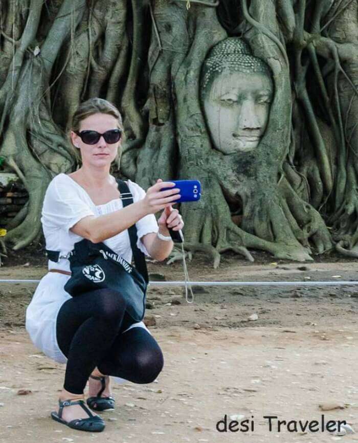 Women posing beside Buddha head in tree roots Thailand