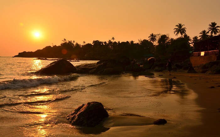 A woman walks on the Palolem Beach as the sun sets in Goa