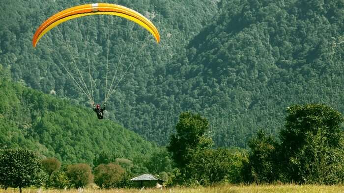 A paraglider lands down amidst the green hills of Bir Billing