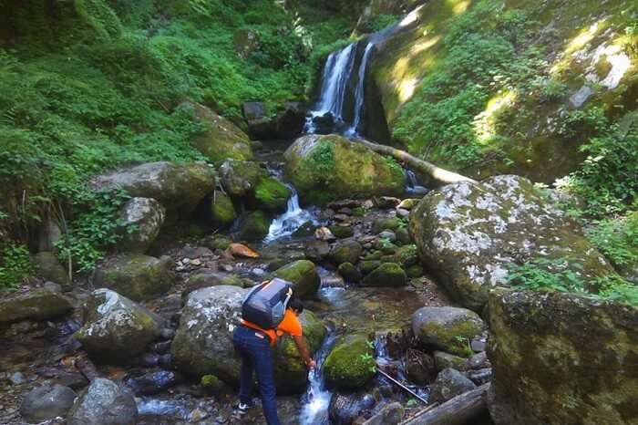 A traveler visits a waterfall near Tirthan Valley