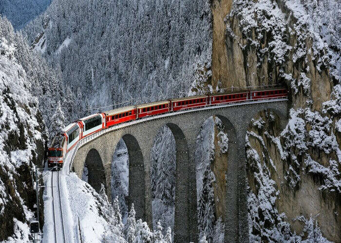 The Glacier Express passing over a bridge through scenic snowy landscapes