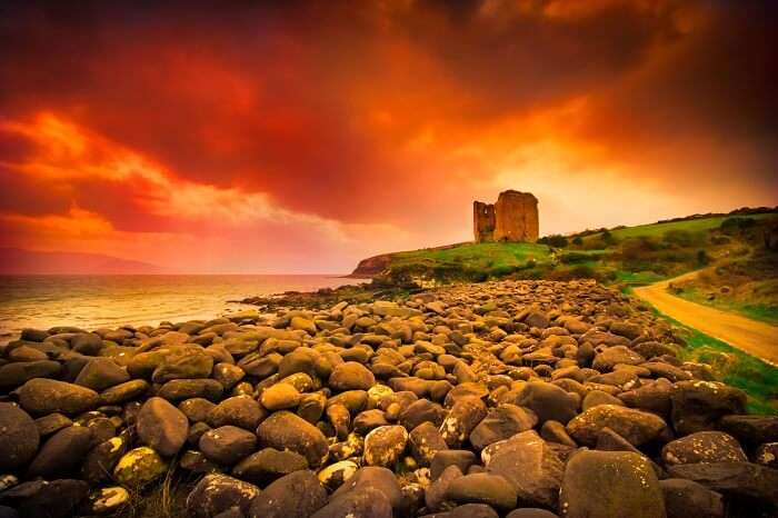 Abandoned medieval Minard castle on Dingle coast in Ireland under dramatic sunset