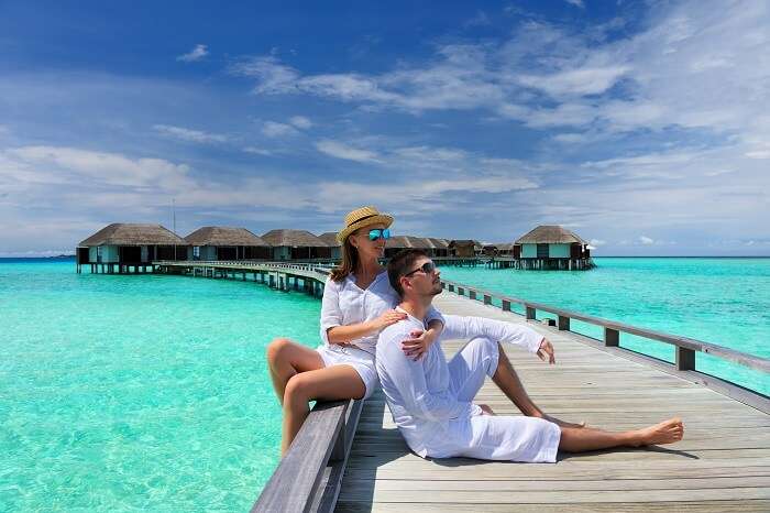 Couple on a tropical beach jetty at Maldives with the over water villas in the backdrop