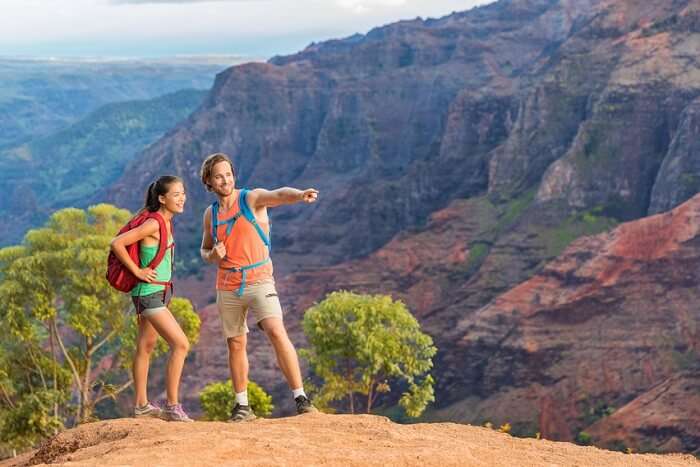 Hiking couple looking at view in mountain nature during hike in Waimea Canyon State Park on the Kauai island in Hawaii