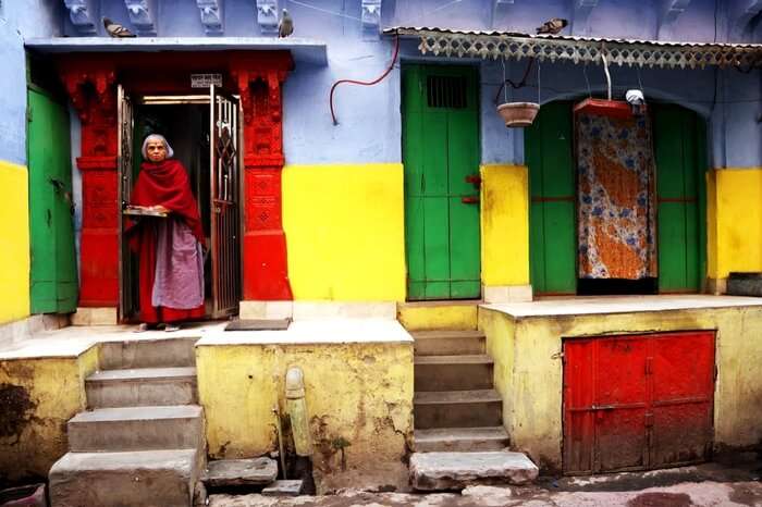 An old woman standing at the door of her colorful home