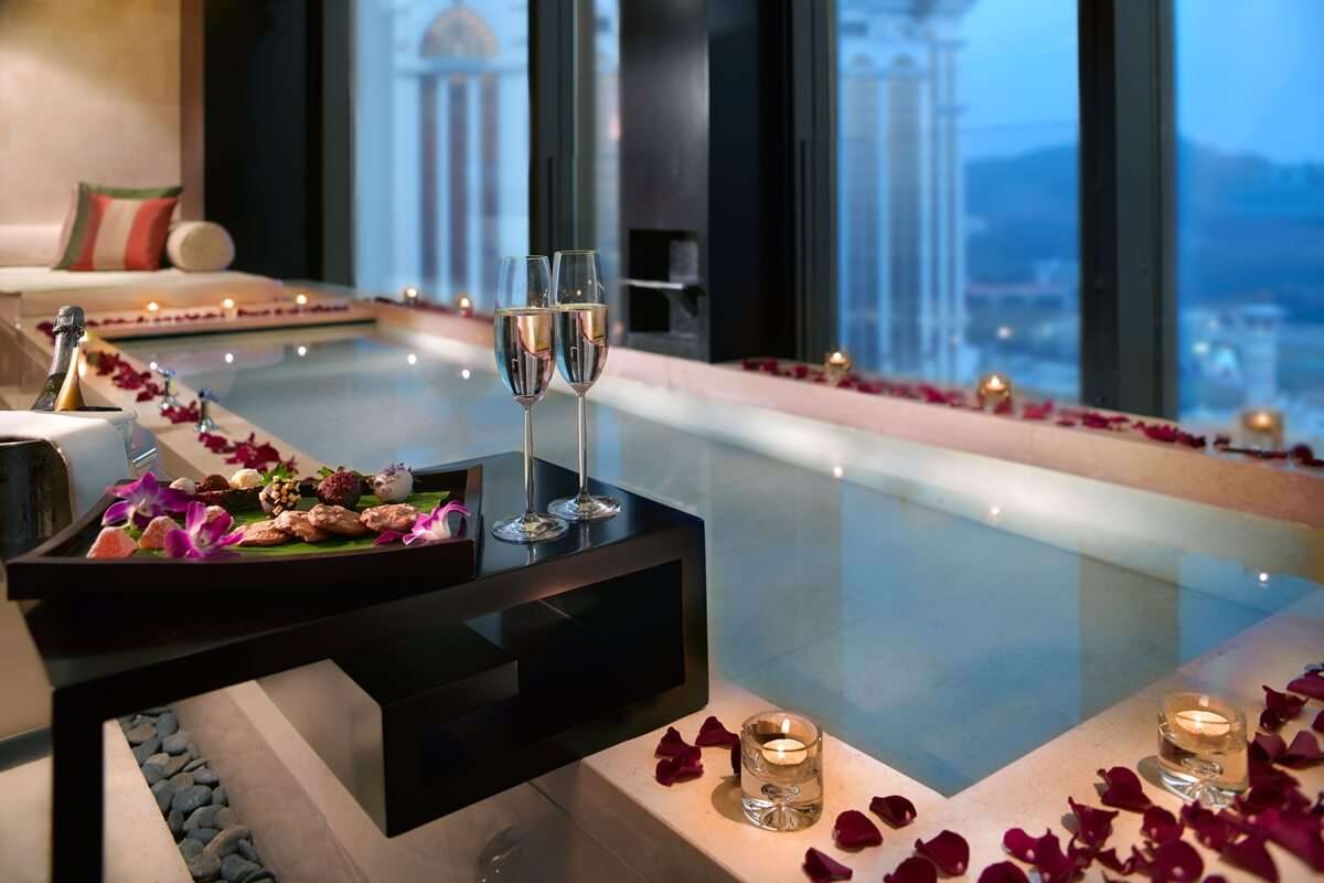 two champagne glasses and bathtub decorated with rose petals