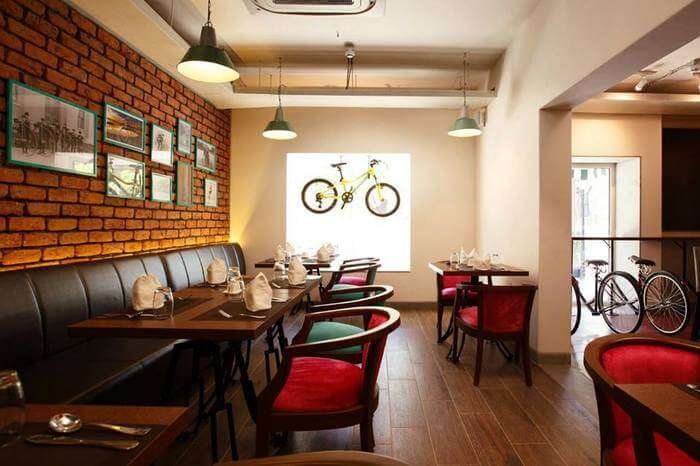 A cycle hung on Mushroom Cafe window Alleppey, Red colour chairs with wooden tables at Mushroom Cafe