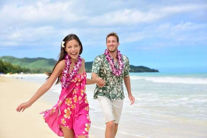 Happy couple having fun on Hawaii beach wearing Aloha shirt and pink sarong sun dress and flower leis