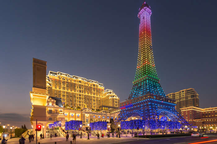 people clicking pictures of Macau Tower decorated with multicolored lights at night