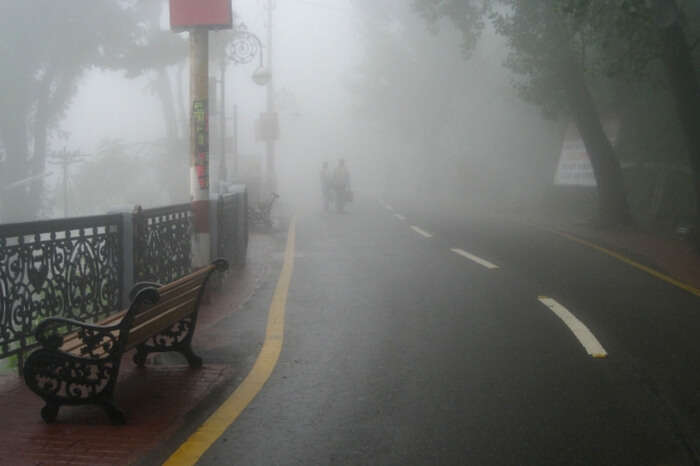 People walking past the Mall Road in Mussoorie on a foggy day