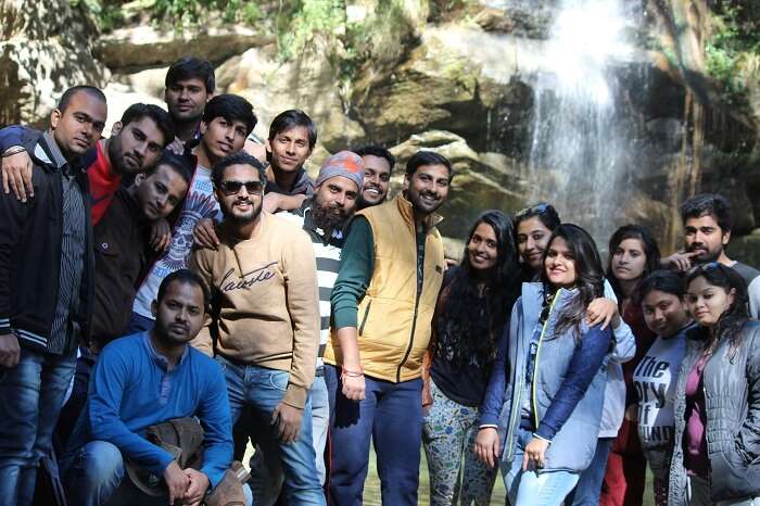 A group of tourists pose in front of a waterfall on their weekend trip to Mukteshwar