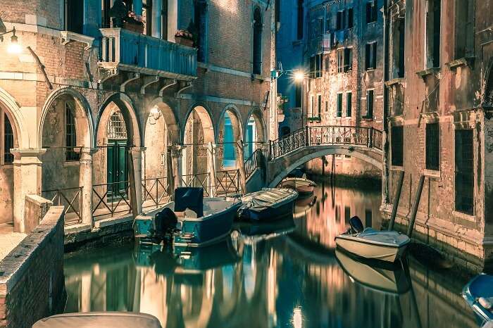 Lateral canal and pedestrian bridge in Venice at night with street light illuminating bridge and houses