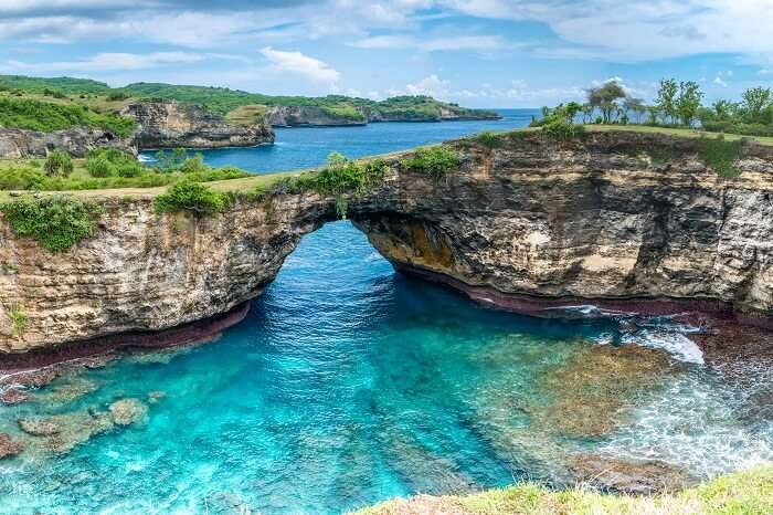 Stone arch over the sea on the rocky beach on the island of Nusa Penida near Bali in Indonesia