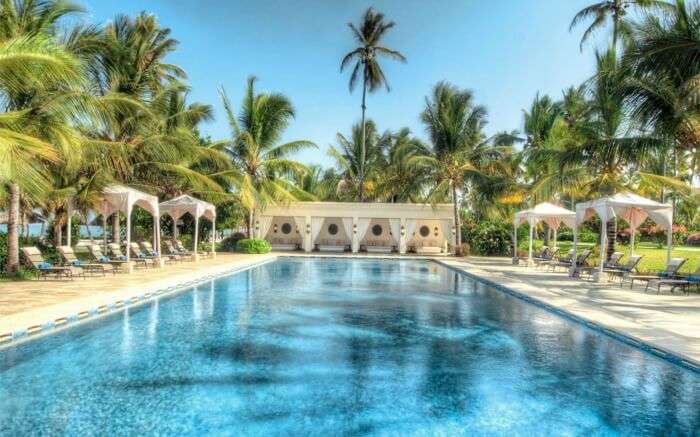 an open pool in a resort with palm trees around it 
