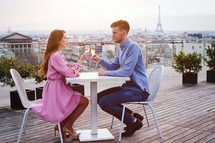 A couple drinking champagne at a luxury rooftop restaurant in Paris on their gourmet honeymoon