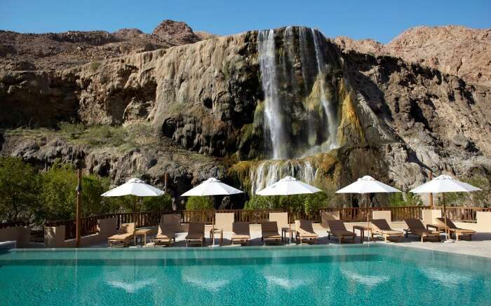 A pool and sun decks with hot spring waterfalls in the background 