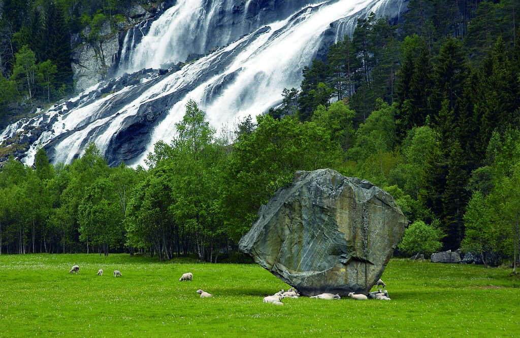 a giant stone on a green field with a waterfall