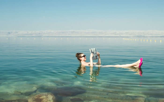 A woman reading newspaper while floating on the waters of Dead Sea