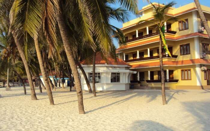 Yellow resort building on a white sand beach surrounded by palm trees 