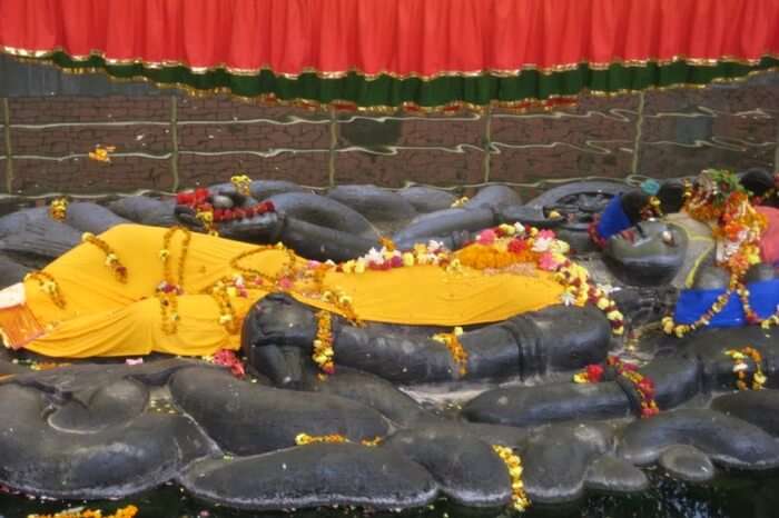 A black stone statue of a god wearing flowers and a yellow sheet