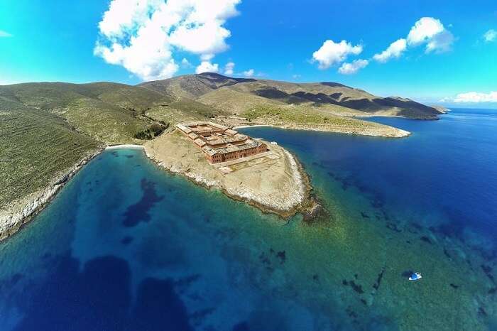 An aerial shot of the prison on the island of Gyaros in Greece along with the azure waters surrounding it