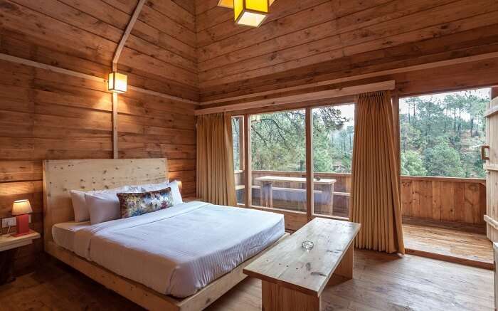 A wooden room with a huge bed and glass windows 