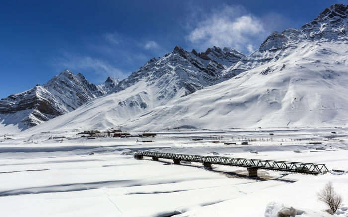 A bridge in Spiti valley overlooked by snow covered mountains