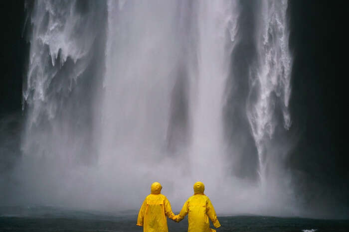 two people standing by a waterfall wearing yellow raincoats