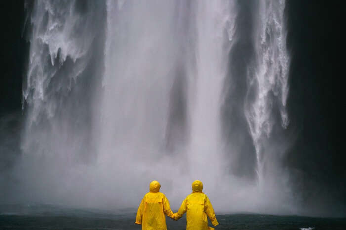 Two people wearing yellow raincoats standing near a waterfall