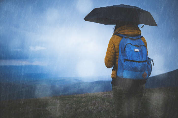 A traveler with a backpack holding an umbrella in the rain on a hill