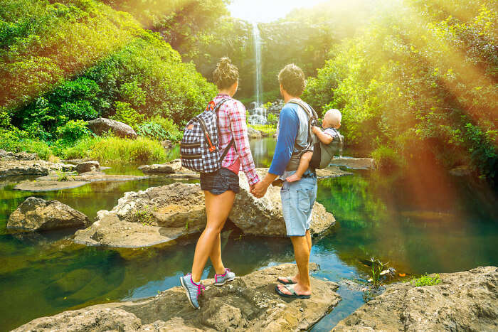 A young couple with their baby, holding hand hand and looking at the waterfall