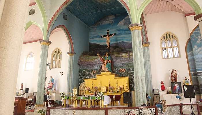 Church altar with Virgin Mary statue haloed by lights, floral decor, saint figures, mural of Jesus, arched window, clock, and painted column at St. Andrew’s Basilica