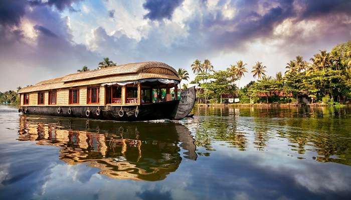 Bateau-maison dans les backwaters près des palmiers au ciel bleu nuageux