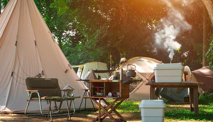 A picture showing a camping tent, kitchen equipment and wooden table set.