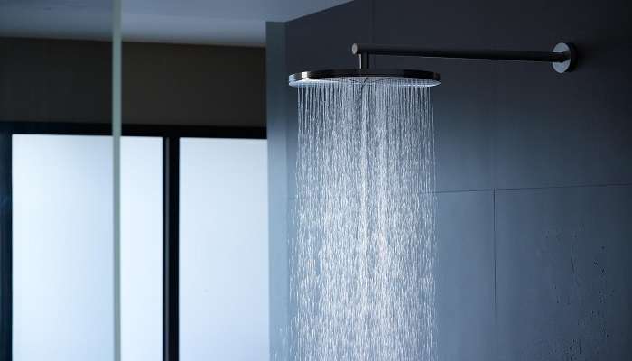 Metal shower head with water running on a black background