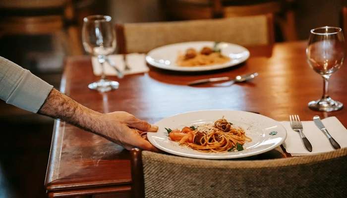 unrecognisable-waiter-serving-pasta-on-table-with-glasses-in-restaurant