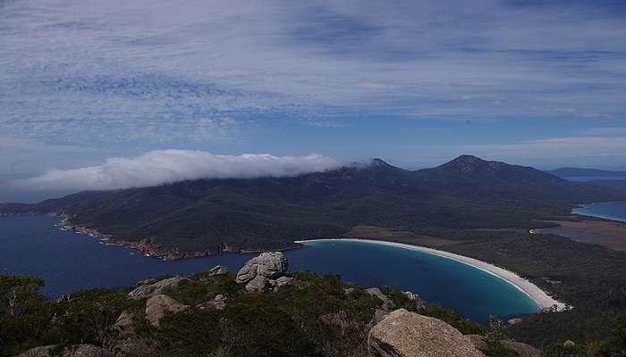  Person capturing a colourful sunset at Honeymoon Bay in Freycinet National Park, with vibrant skies and calm waters in the background.