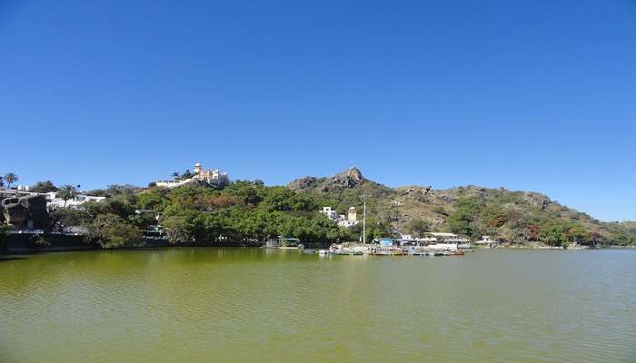 Row of boats afloat on Nakki Lake's serene surface with surrounding hills to visit near Trevor’s Tank.