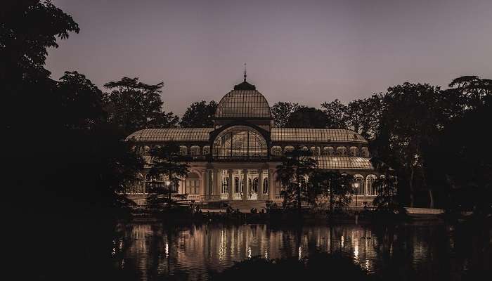 The Crystal Palace at El Retiro Park reflects in the lake.