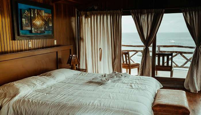 White Bed Linen Near Brown Wooden Bed Frame with beach-side view