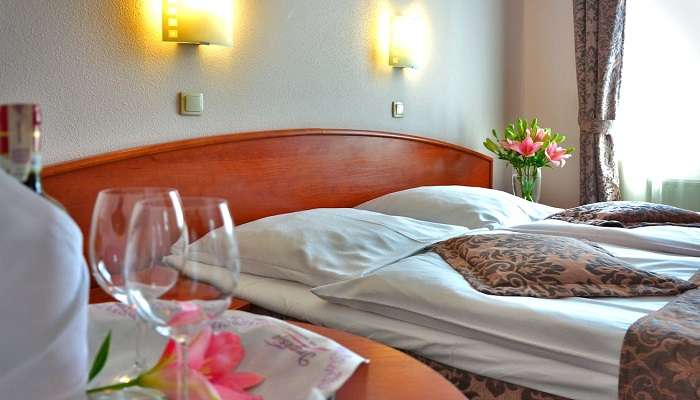 Clear Wine Glass on Brown Wooden Table Top Near Bed in the hotel