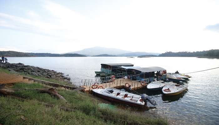 Boat rides on the calm water of Banasura Sagar Dam at the backdrop of the hills covered with green vegetation.