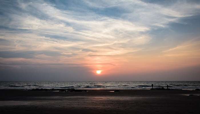 Serene Ashwem Beach at sunset, with golden sand, still water, and palm trees along the beach line silhouetted against the sky near the Palm Sweet Water Lake.