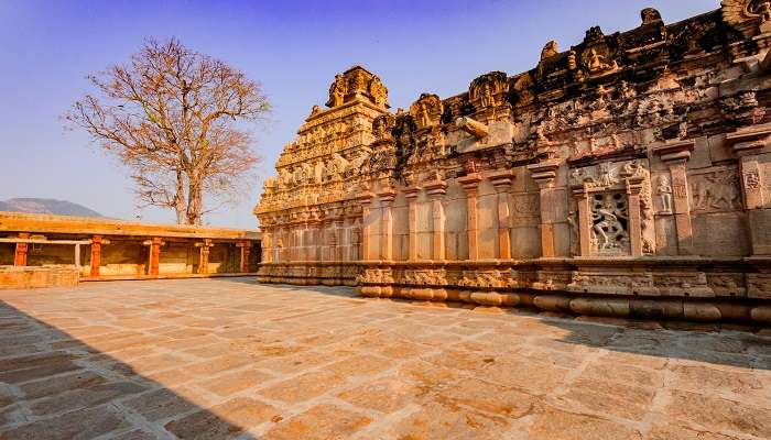  Intricate Dravidian architecture of Bhoga Nandeeshwara Temple with elaborated stone carvings inside it; ancient trees surround it.