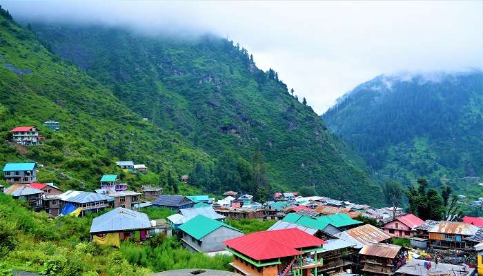 Malana village traditional wooden houses with snow-capped peaks in the background 